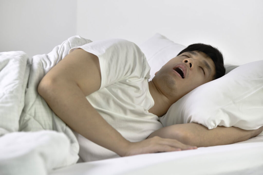 Young man snoring loudly while asleep in bed